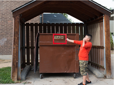 child holding nose in front of a trash can